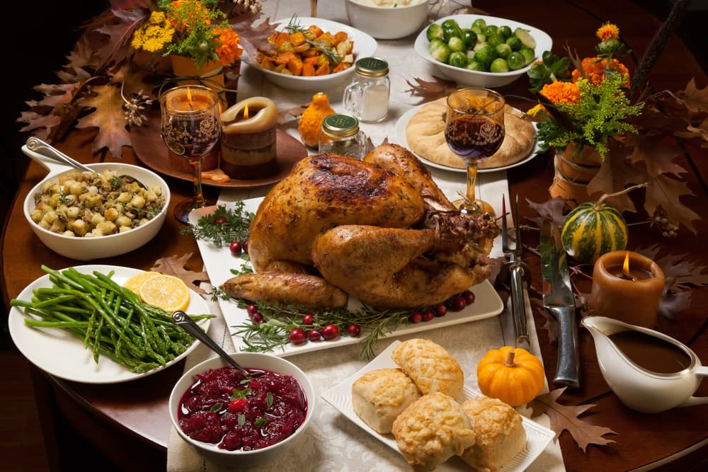 Thanksgiving dinner spread with roast turkey, side dishes, and lit candles on a table