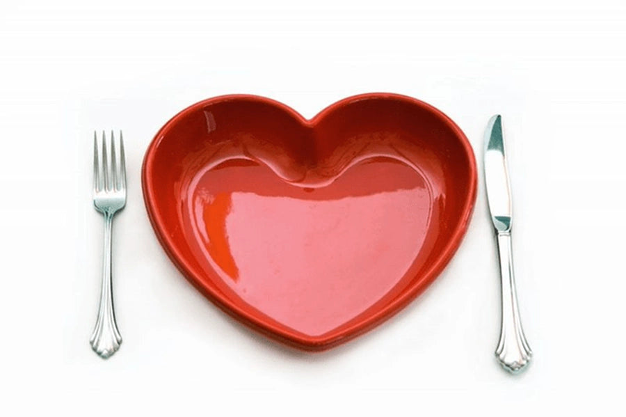 Red heart-shaped dish placed between a fork and knife on a white background