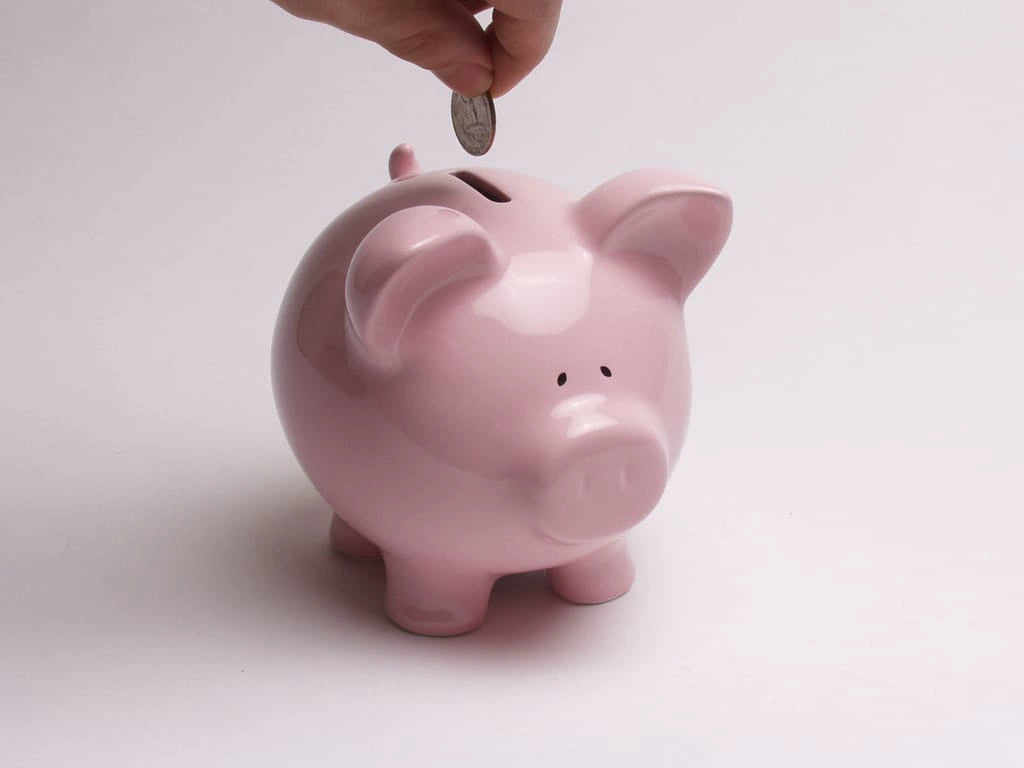 Hand dropping a coin into a pink piggy bank