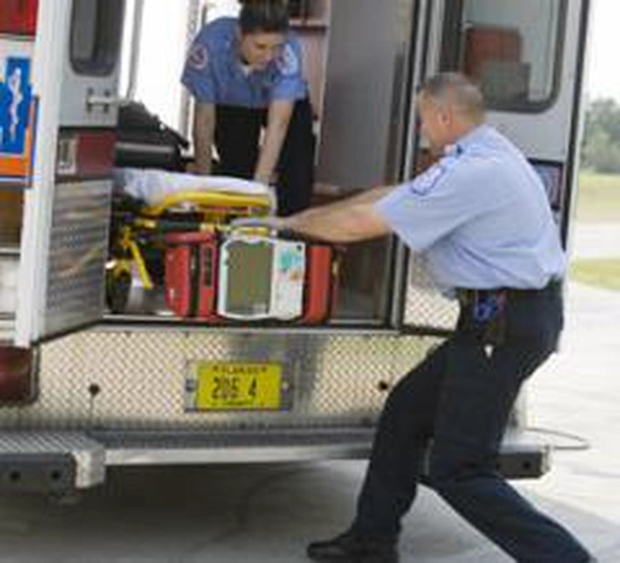 Two EMS paramedics loading a gurney with an AED into an ambulance