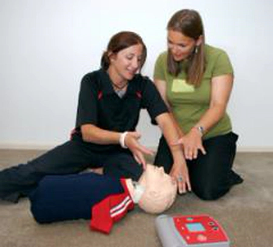 Two women practicing CPR on a training manikin with an AED nearby