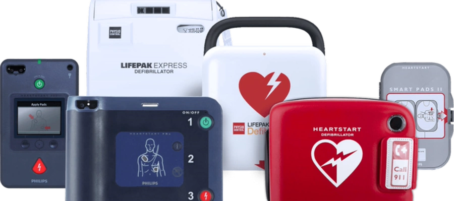 Lineup of AED defibrillators including HeartSine, Defibtech Lifeline, Cardiac Science Powerheart, Physio-Control Lifepak, ZOLL, and Philips HeartStart