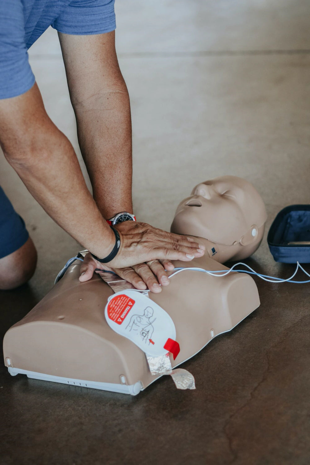 Person performing chest compressions on a CPR training manikin next to an AED trainer