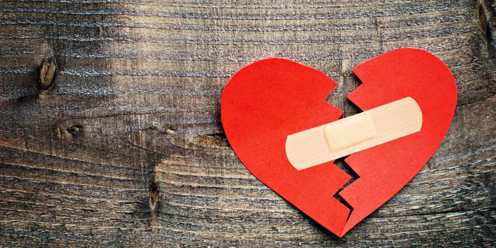 Paper heart cut in two pieces mended with a bandage on a wooden surface