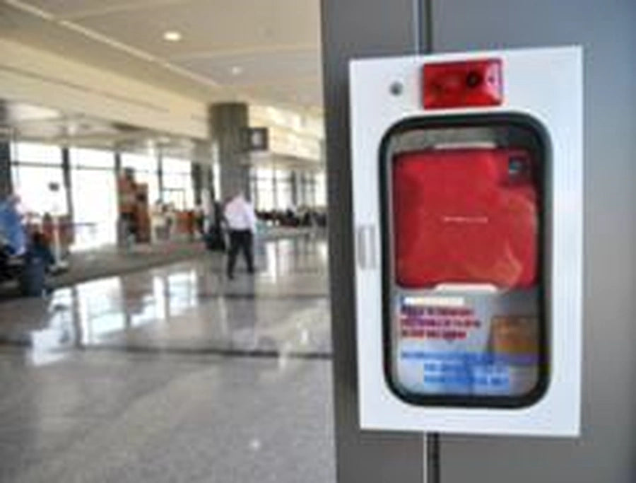 AED wall cabinet in a public terminal with red carrying case visible