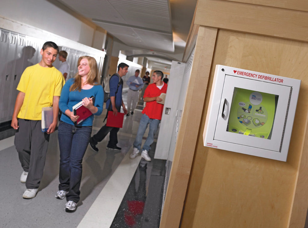 Students walking past a wall-mounted emergency AED cabinet in a school hallway