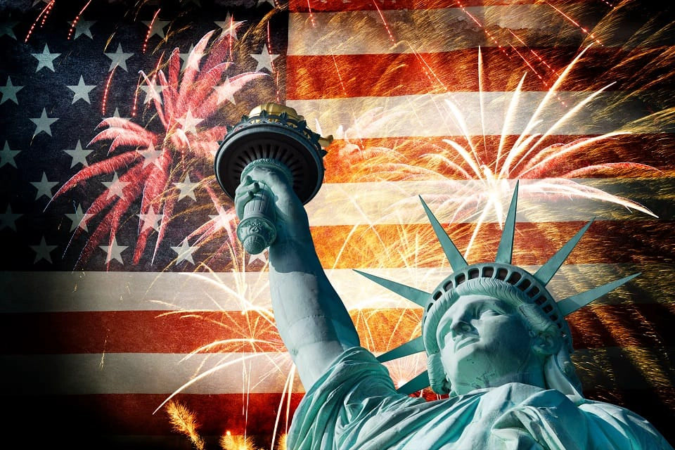 Statue of Liberty torch and crown silhouetted against an American flag with fireworks bursting overhead