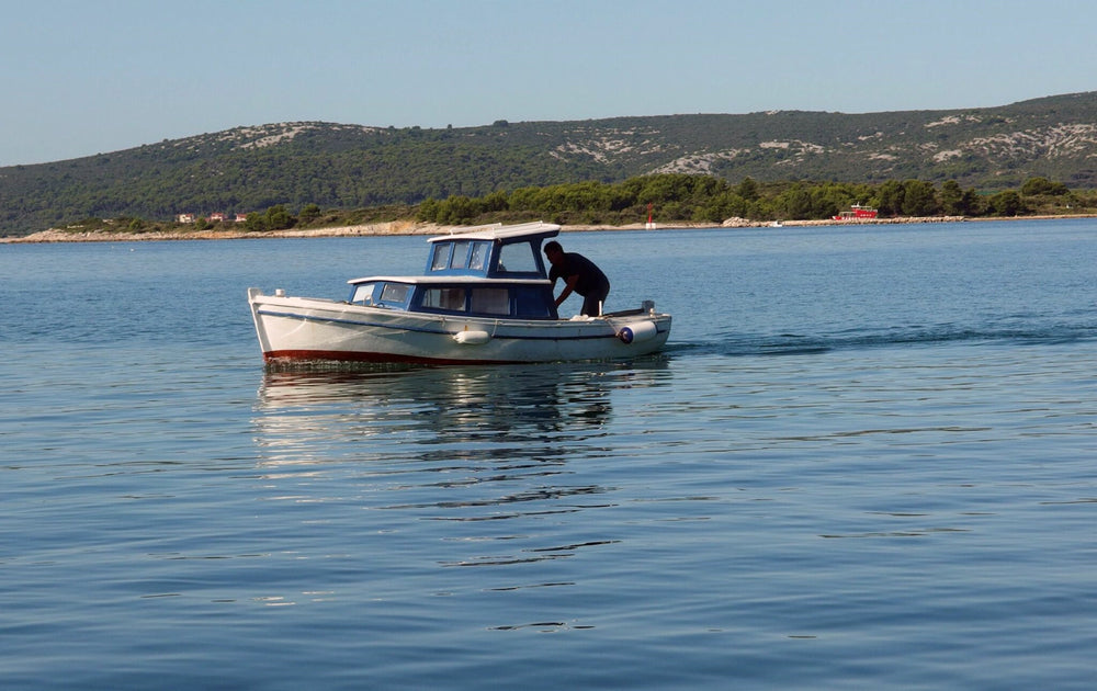 Man working on a small white and blue boat on calm coastal waters