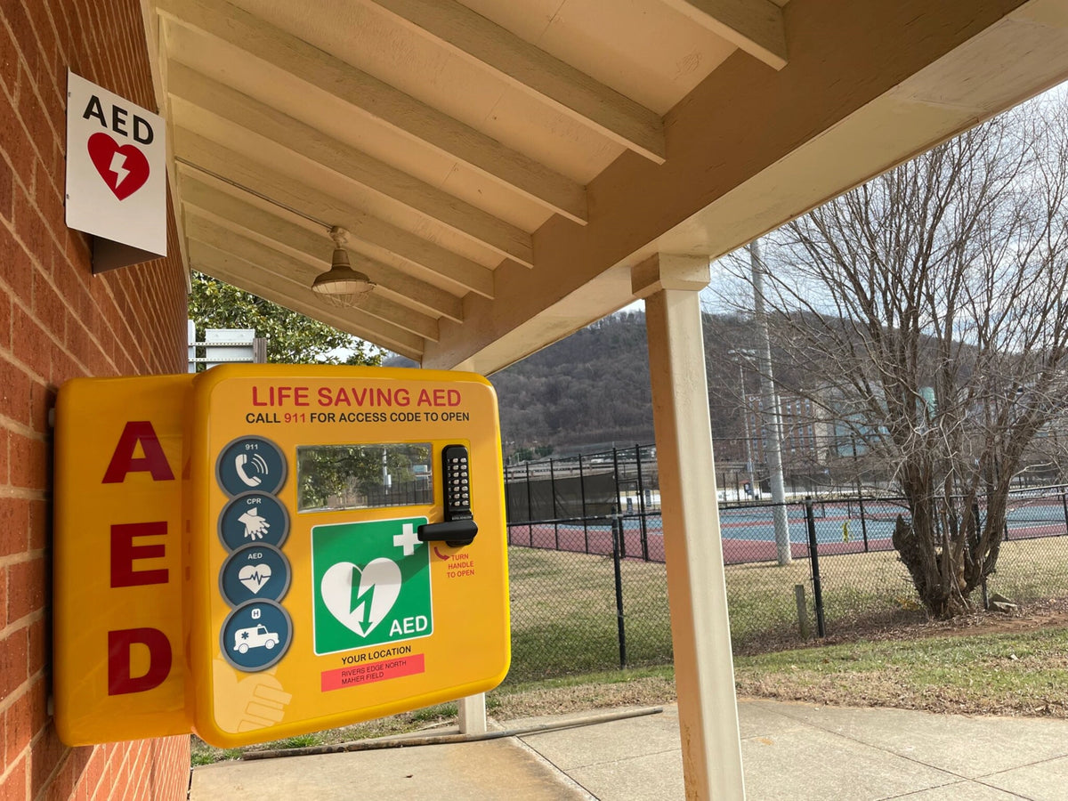 Yellow wall-mounted Life Saving AED cabinet with keypad mounted on a brick building exterior