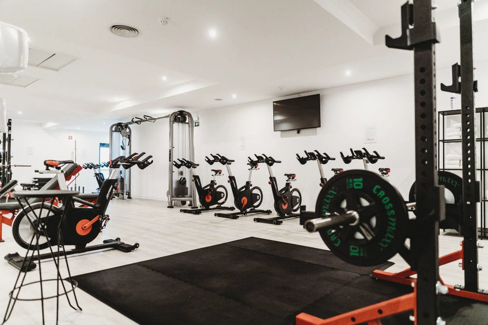 Empty modern gym interior with exercise bikes, weight racks, and a wall-mounted TV