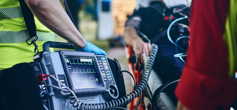 Paramedic's hand resting on a portable cardiac monitor and defibrillator screen showing heart rhythm