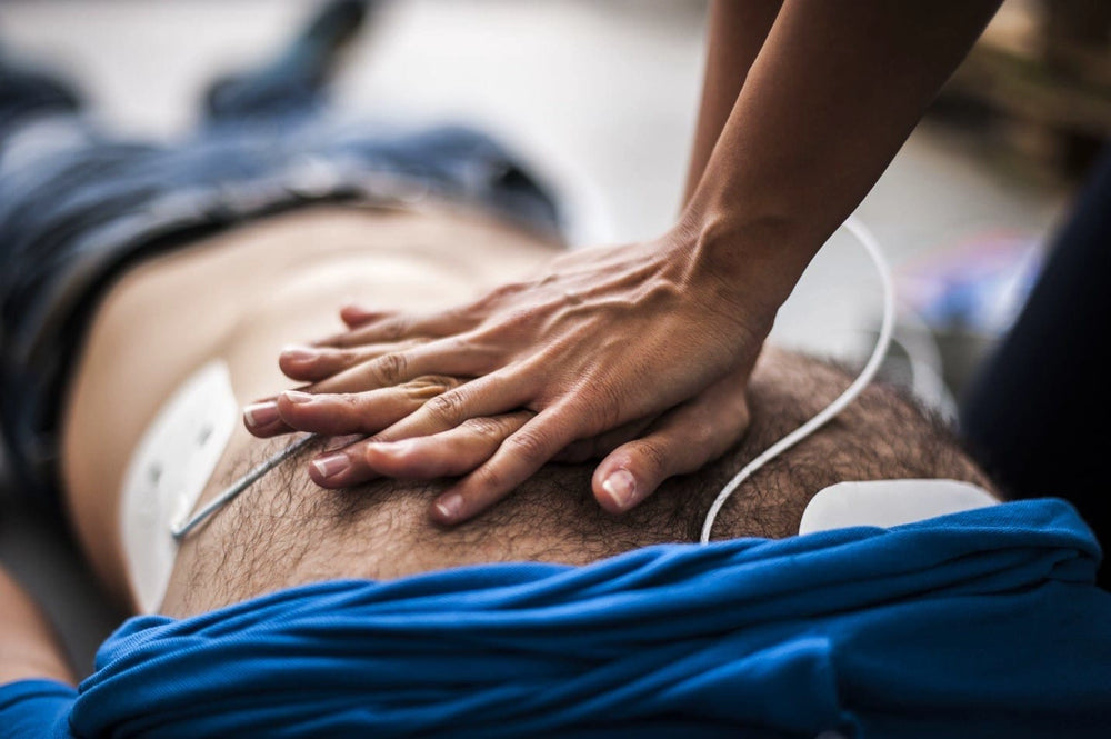 Close-up of rescuer's hands performing chest compressions with AED pads attached to a patient's chest
