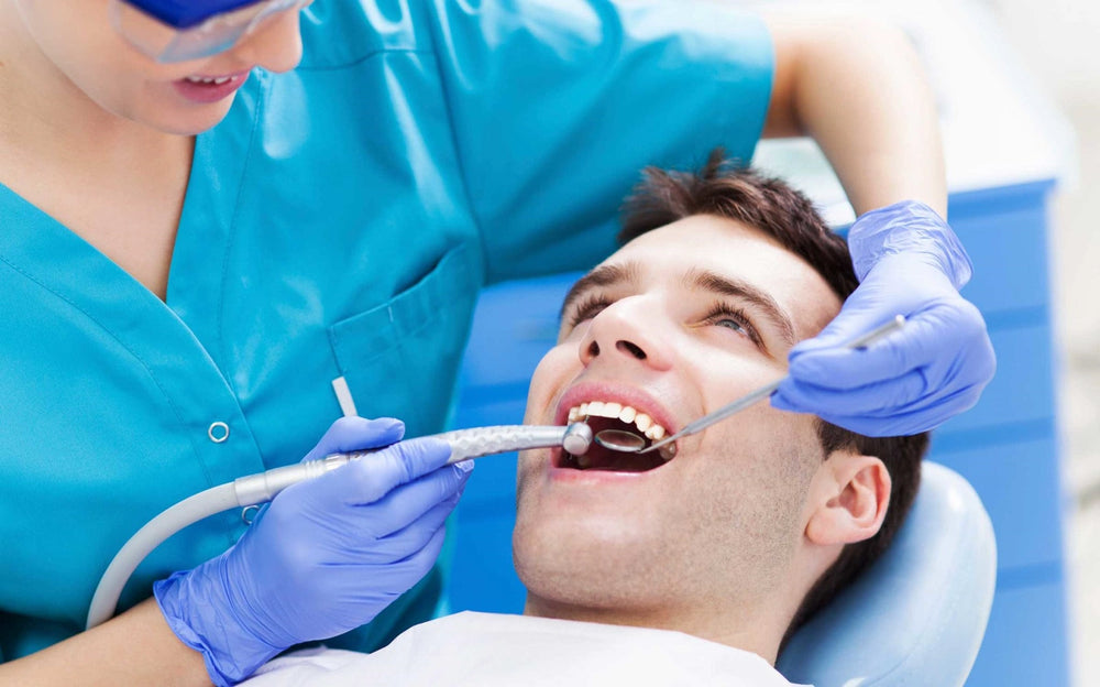 Dentist in blue scrubs and gloves examining a patient's teeth with dental tools