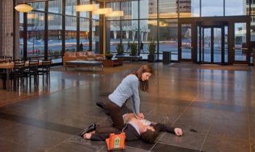 woman using AED on man in office building lobby