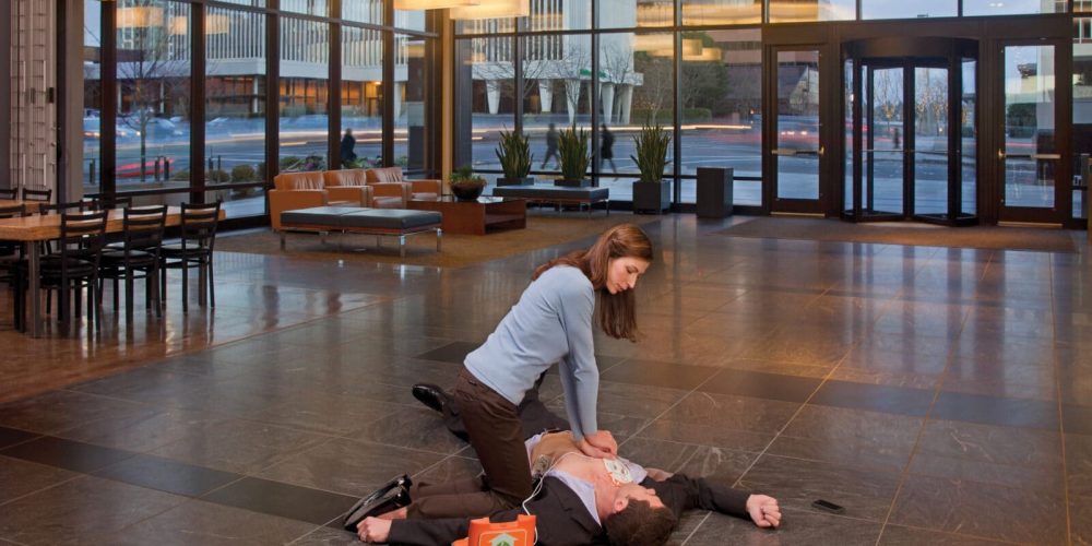 woman using AED on man in office building lobby